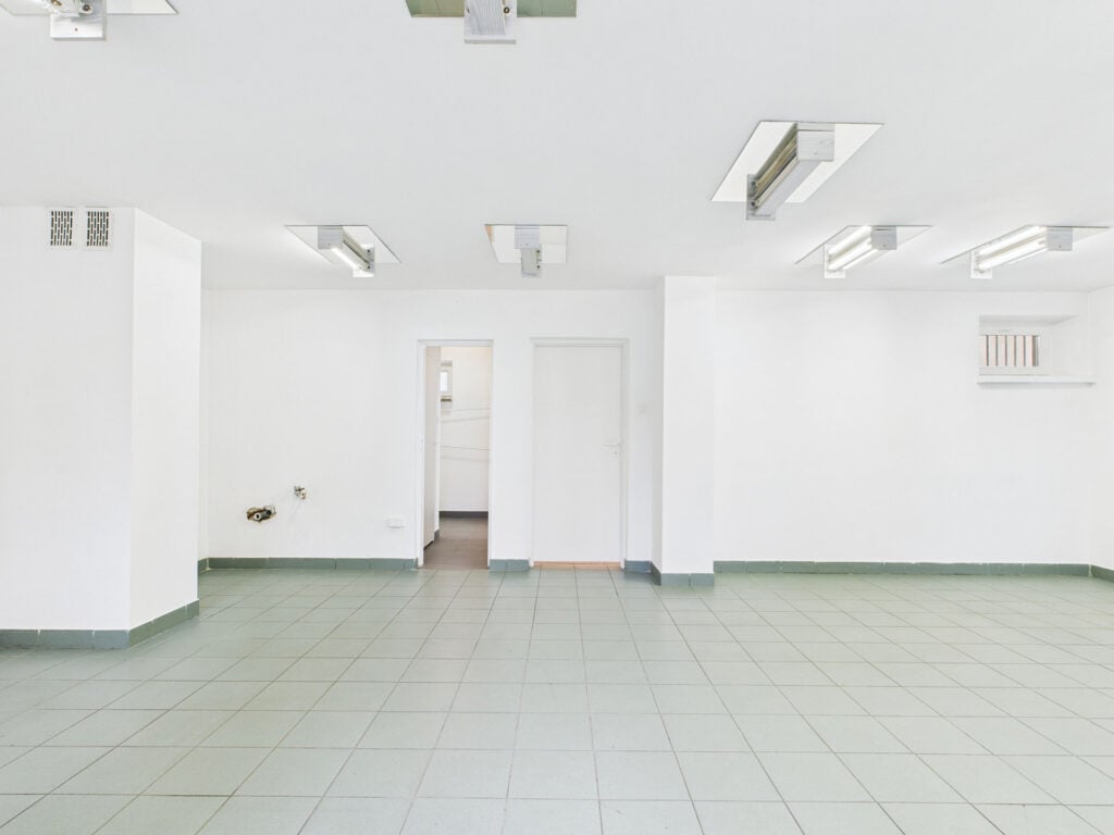 Pusta biała przestrzeń z kafelkami i światłami sufitowymi.