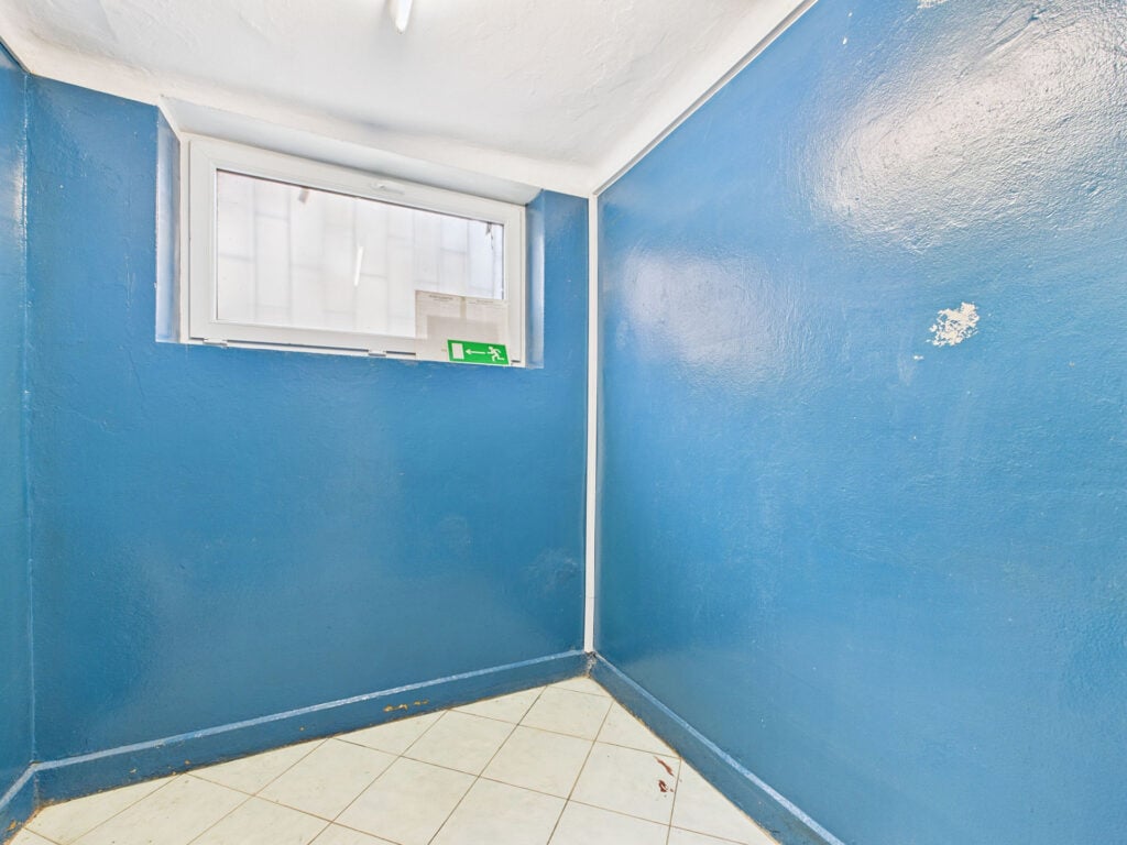 Niebieski pokój z oknem i znak wyjścia awaryjnego.