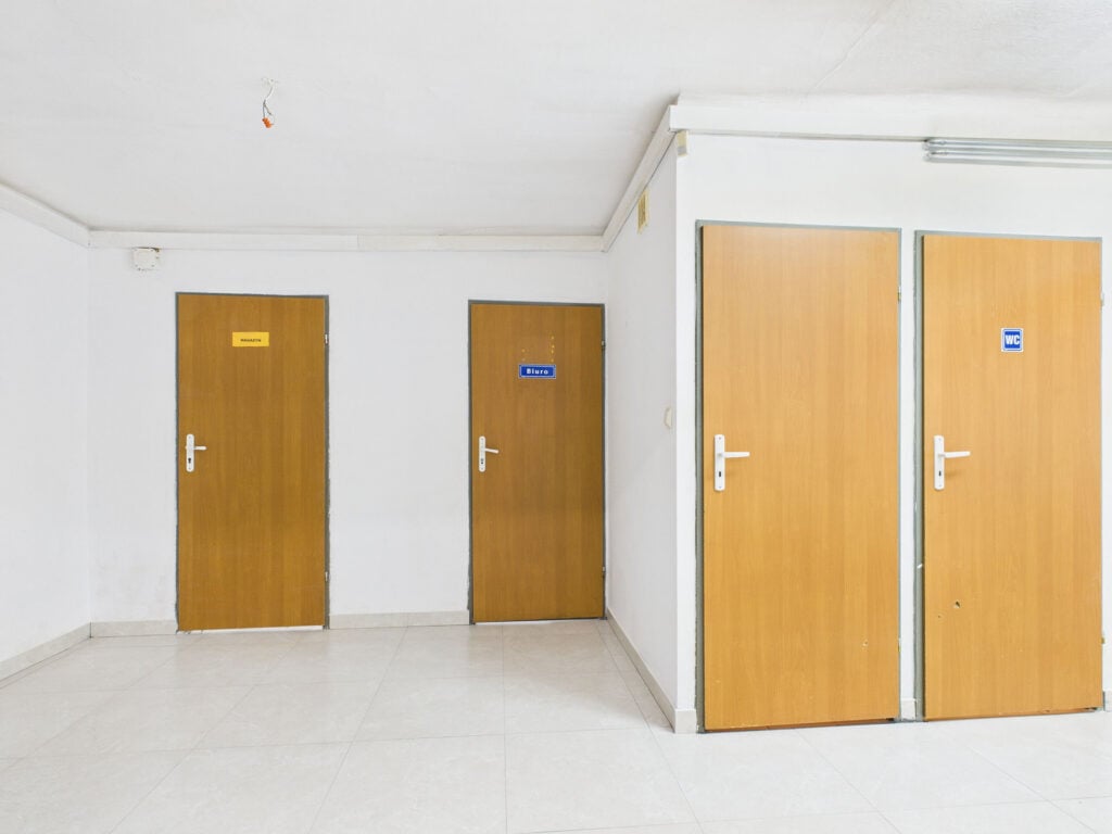 Trzy brązowe drzwi z oznaczeniami: biuro, magazyn, WC.