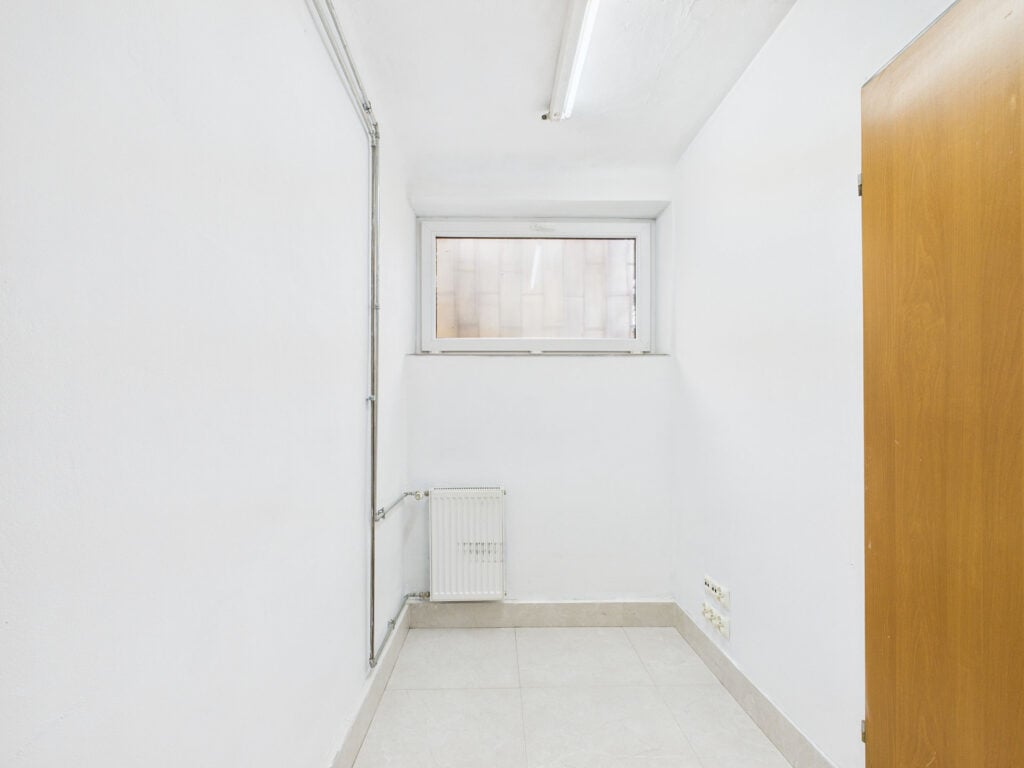 Małe pomieszczenie z oknem, kaloryferem i drzwiami.