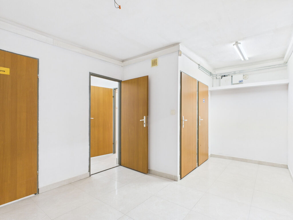 Korytarz z białymi ścianami i drewnianymi drzwiami.