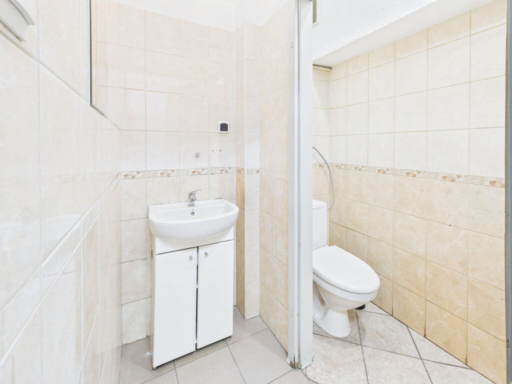 Łazienka z umywalką i toaletą, jasne kafelki.