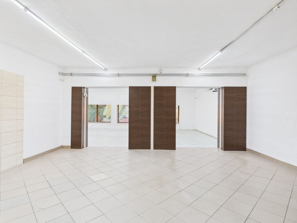 Pusty pokój z płytkami podłogowymi i drewnianymi drzwiami.