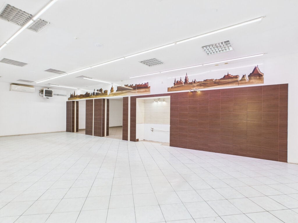 Puste pomieszczenie z białymi płytkami i ozdobną boazerią.