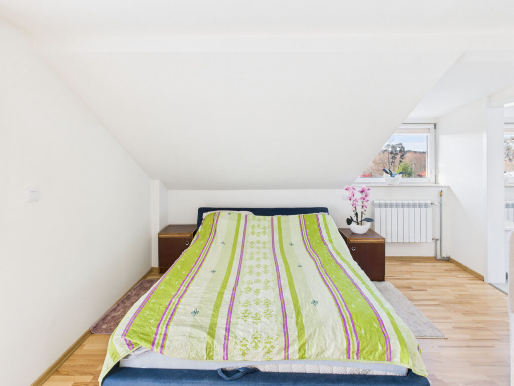 Sypialnia na poddaszu z zieloną pościelą i kwiatami.