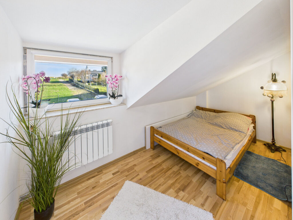 Przytulna sypialnia na poddaszu z widokiem na ogród.