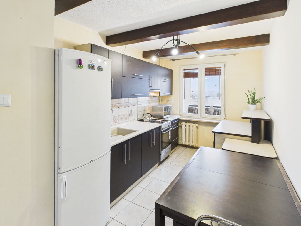 Jasna kuchnia z oknem i ciemnymi szafkami.