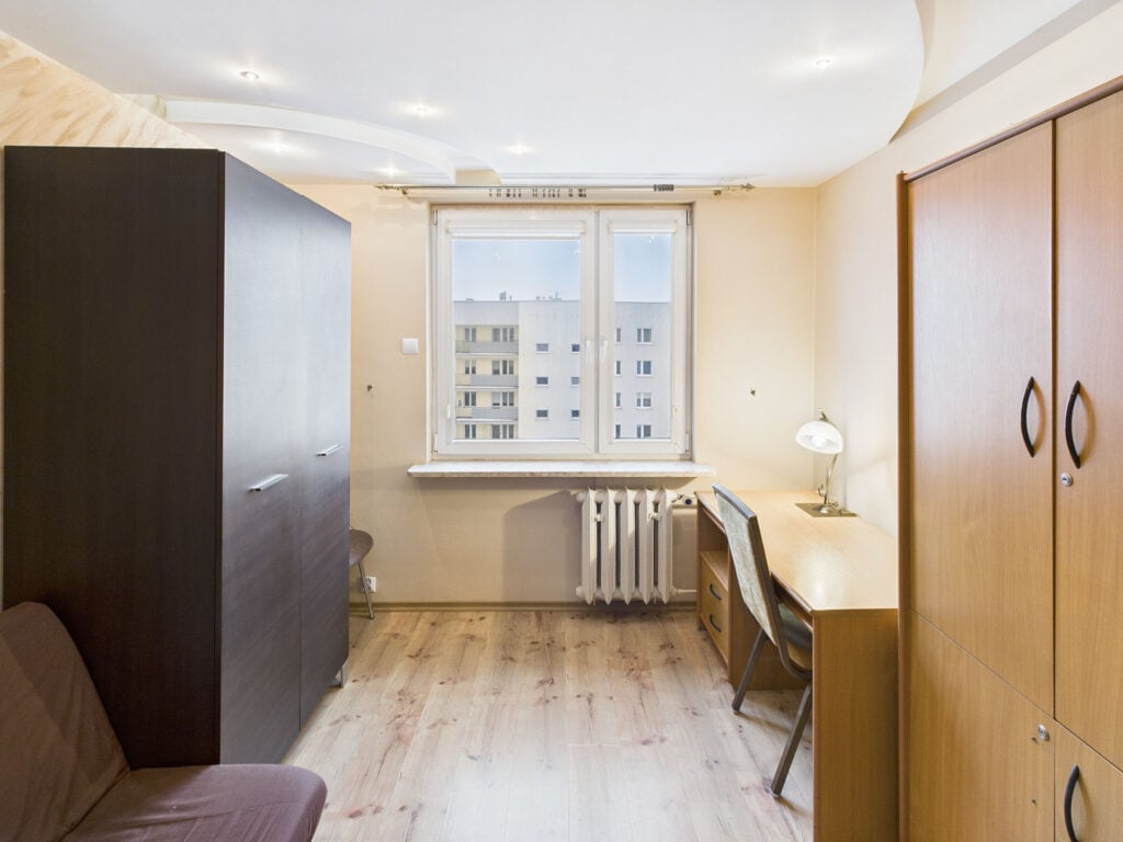 Pokój z biurkiem, szafą i widokiem na blok.