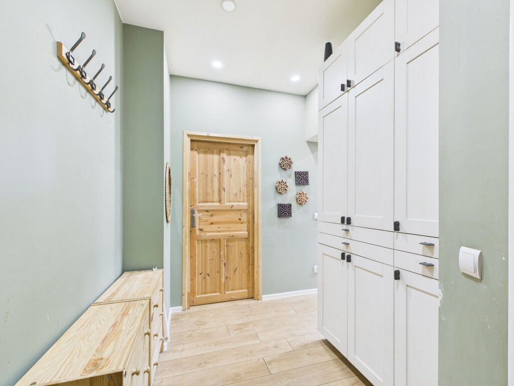 Przedpokój z białymi szafkami i drewnianymi drzwiami.
