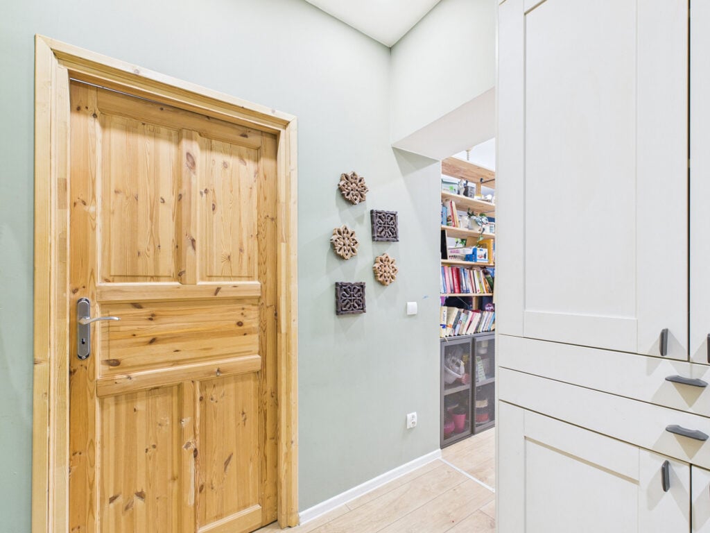 Drewniane drzwi, ściana z dekoracją i regał z książkami.