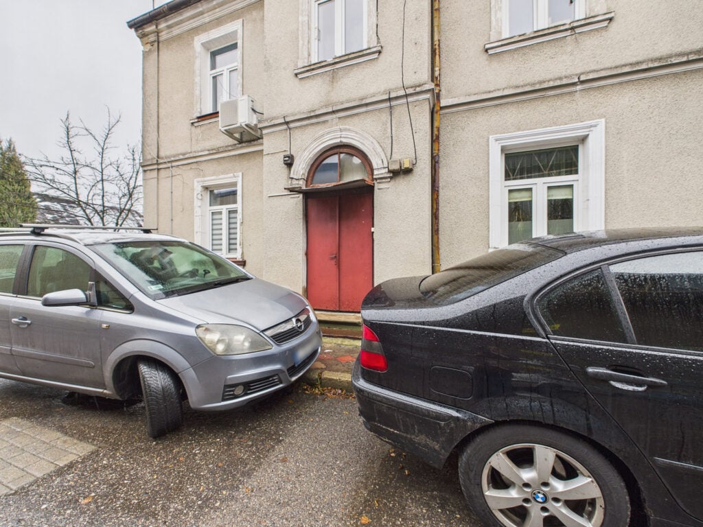 Parkujące samochody przed budynkiem w deszczowy dzień.