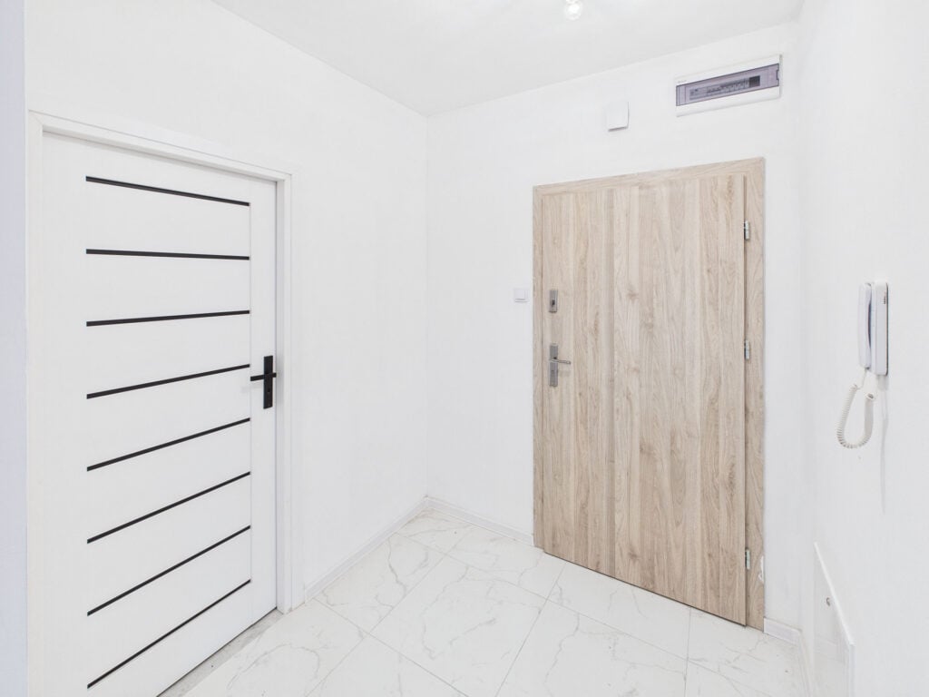 Minimalistyczny biały przedpokój z drewnianymi drzwiami