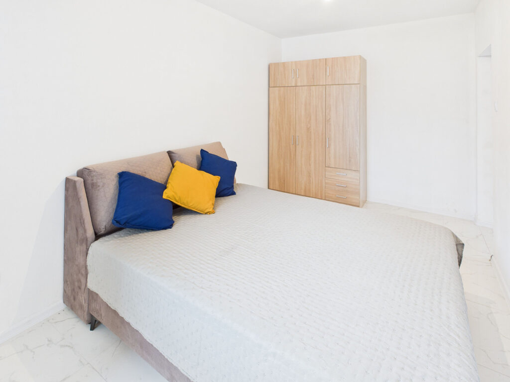 Jasna sypialnia z łóżkiem i szafą.