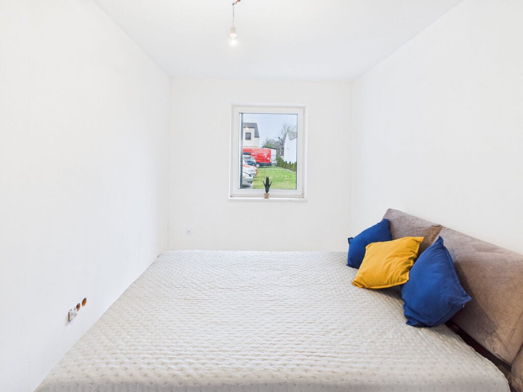 Jasna sypialnia z łóżkiem i poduszkami, widok na ogród.