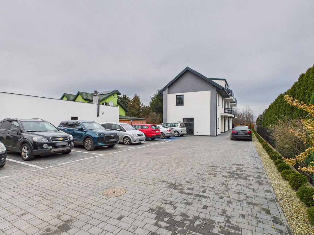 Parking z samochodami obok budynku mieszkalnego.