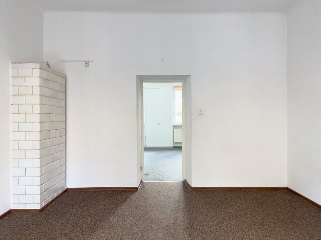 Puste pomieszczenie z białymi ścianami i piecem kaflowym.