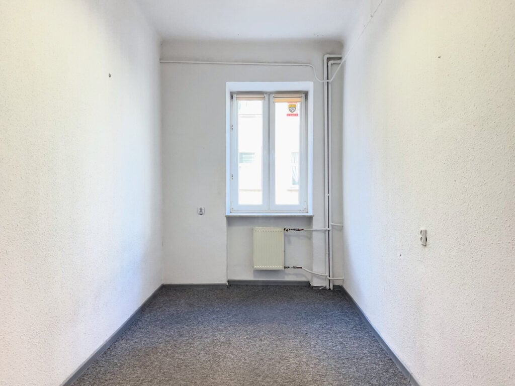 Puste białe pomieszczenie z oknem i grzejnikiem.