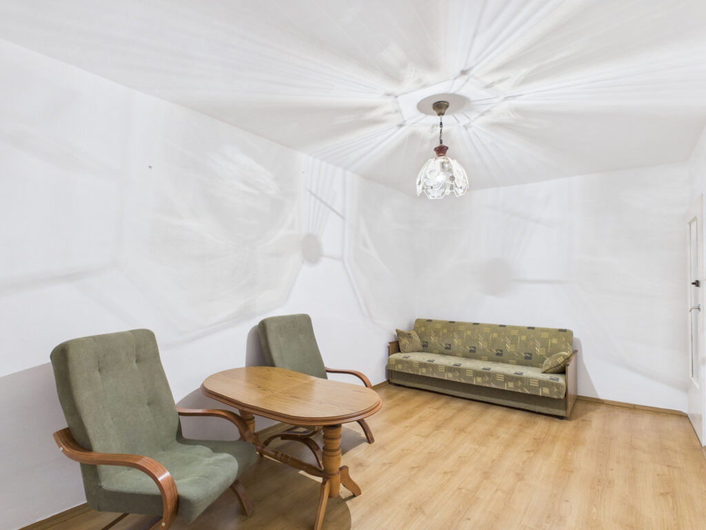 Pokój z sofą, fotelami, stołem i lampą sufitową.