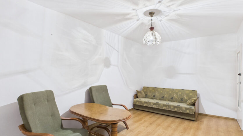 Pokój z sofą, fotelami, stołem i lampą sufitową.