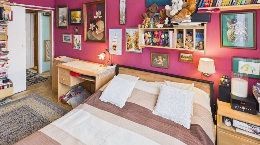 Przytulna sypialnia z książkami i obrazami na ścianie.